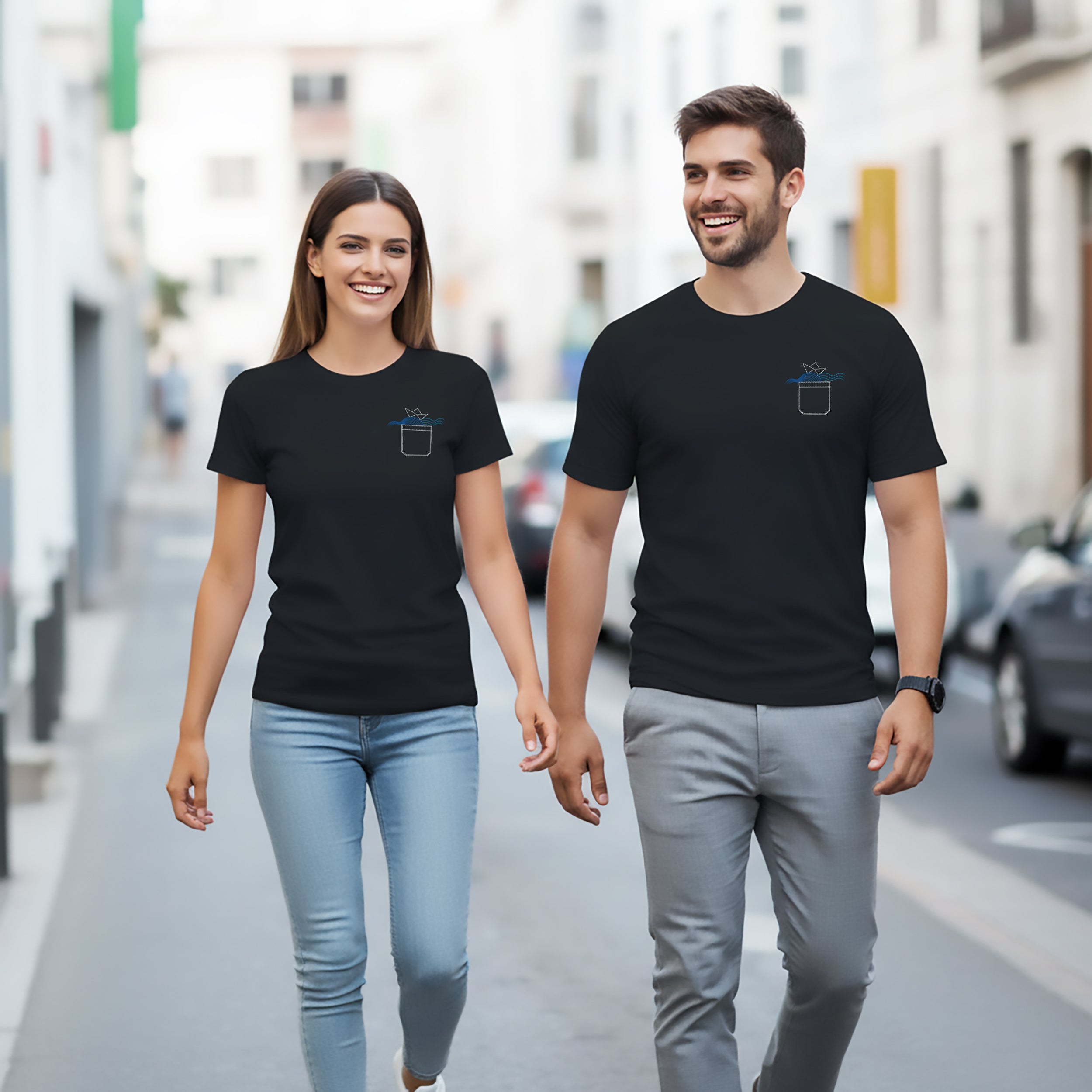 Two people walking hand in hand on a city street wearing black t-shirts with an origami Boat on a pocket design.