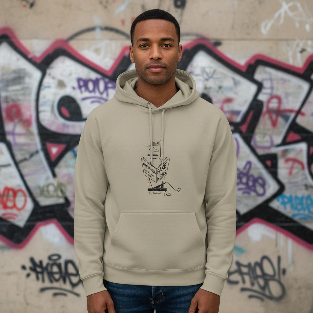 Man wearing a beige hoodie with a graphic design in front of a graffiti-covered wall.